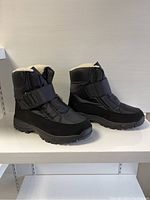 Side view of black winter boots showing the rubber sole, fleece interior lining, and Velcro strap closure.