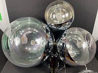 Photo showing three acrylic pendant globes of different sizes with reflective chrome-like inner surfaces and clear outer shells, placed around a bottle for scale.
