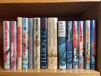 Photo of 15 vintage Dudley Pope books with dust jackets, titles visible on spines, arranged vertically on a wooden shelf.