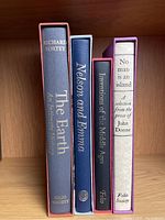 Four Folio Society books standing on a wood shelf, with visible titles on spines and slipcases.