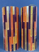 Pair of cylindrical Mid-Century Modern lamp shades with vertical lucite strips in colored segments photographed side-by-side against a black background.