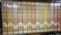 A shelf view showing the spines of the 14 volumes in the Enciclopedia de México set with a continuous white Quetzalcoatl serpent design across them.