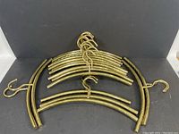 Full set of 17 brass hangers arranged on dark background showing curved shape and attached hooks.