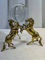 Front view of three brass horses rearing and supporting a clear crystal ball, showing overall design and size.