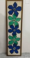 Full frontal view of tall narrow painting showing six stylized flowers in alternating blue and green on off-white background, containing gold-tone wood frame