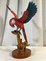 Full view of the red and blue carved wooden parrot mounted on a natural wood branch and round wooden base.