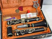 Full view of clarinet pieces and accessories inside orange lined, black hard case. Shows parts of clarinet laid out and accessory arrangement.