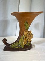 Front angle view of the vintage Roseville cornucopia vase showing the shape, textured surface, and floral decoration.