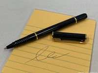 Vintage Waterman ballpoint pen resting on a yellow lined notepad, showing pen and detached cap.