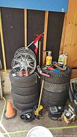 Two stacks of winter tires with rims, car chemicals, and tools in a garage corner.