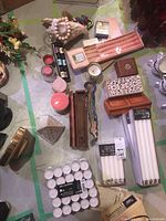 Photo showing multiple candles including tea lights, taper candles both pink and white, wooden and glass candle holders, carved trinket boxes, and a white conch shell.