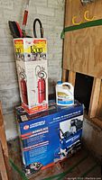 Boxed Campbell Hausfeld 8 gallon air compressor kit along with Chapin concrete sprayer and water guard jug on the floor against a wall.