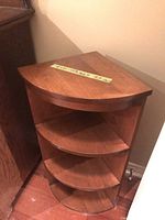 Photo of the wooden corner shelving cabinet with three curved shelves, brown finish, tagged with measurements.