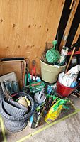 Overview of gardening lot showing multiple planters, watering hose, hand tools, a green watering wand, plant trays, Miracle-Gro fertilizer, and other gardening supplies.