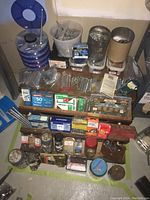 Wide shot showing multiple shelves with containers holding screws, nails, fasteners, small jars, toolbox sections, and boxed hardware supplies.