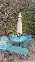 Overview of teal wrought iron patio set with oval table, six chairs, chaise lounge and closed umbrella