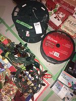 Three strings of Christmas lights, including a black reel spool of For Living brand warm white string lights and two loose strings of multi-colored Christmas lights on green wires.