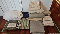 All assorted linens including duvet cover, pillowcases, sheets in various colors and patterns folded on wooden floor.