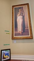 Framed print on stretched canvas depicting a classical figure, shown hanging on cream wall, visible barcode tags near bottom edge