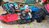 Photo showing the full lot including two snowboards with bindings, three helmets, black snow pants, blue jacket, red neck warmer, and black snowboard bags.
