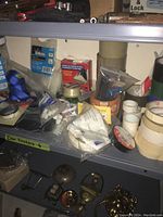 Shelving unit with assorted rolls of masking tape, black insulating tape, and magnetic tape fasteners along with other packing materials and supplies.