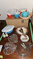 Overview of vintage Pyrex mixing bowls stacked on a cardboard box with other kitchen items including glass dishes and salt shakers.