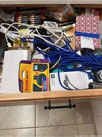 Wooden drawer with Kodak Max battery charger, tangled power cables, blue cables, digital multimeter, small pouch, batteries, and miscellaneous small electronics