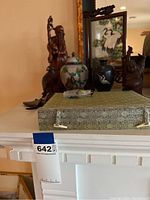 Overall display of the Asian art collection showing wooden figurine, cloisonné and blue vases, small carvings, framed crane painting, and snuff bottle box