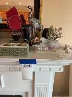 Overall view of the Asian art collection showing cloisonné crane, boat, marble figurines, mug, and floral decorative item arranged on a mantel.