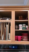 Photo showing vertical arrangement of baking sheets and cutting boards alongside bowls and teapot inside wooden cabinet.
