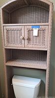 Full view of the wicker over toilet shelf showing woven wicker cabinet with two doors and two shelves above and around a toilet tank.