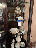 Crystal glasses displayed on top shelf with Nippon vase and white ceramic soup spoons also visible.