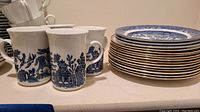 Blue and white patterned mugs and stack of plates showing the dinnerware pattern and quantity