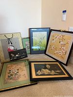 Photo shows all seven framed Asian artworks grouped on carpeted floor, showcasing variety of themes and frames.