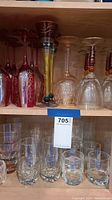 Red and yellow decorative goblets, clear wine glasses, assorted crystal-cut tumblers on a wooden shelf