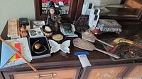 Wide view on dresser top showing all miscellaneous items including doll, jewelry, butterfly dish, decorative egg, gold-toned box, Zippo lighter, and handheld game.