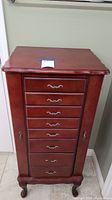 Full front view of red-brown wooden jewelry cabinet on four carved legs