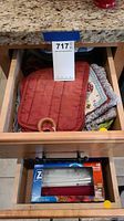 Open drawer showing red quilted potholder with wooden ring on top and assorted cloth towels beneath.