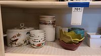First photo showing white ceramic containers with floral designs, floral bowls stacked, and ceramic leaf bowls on shelf.