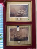 Two framed nautical paintings with ships sailing on the ocean in gold-tone frames hanging on a red wall.