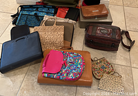 Top-down view of numerous assorted purses and bags arranged on tiled floor including Dooney & Bourke purse, colorful patterned purses, cashbox, and small velvet boxes