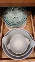 Clear glass nesting Pyrex bowls and white ceramic casserole dishes stacked in a drawer