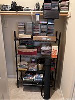 Full view of black metal shelving unit containing stacks of CDs, VHS tapes, greeting cards, boxes, and other miscellaneous items.