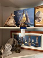 Two shelves with various nautical decor, including shells, framed knots, miniature ship, framed yacht photo, book on America's Cup, and brass lantern.