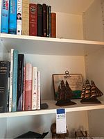 Bookshelf shelf showing books and two bronze metal sailing ship sculptures with a framed card description behind them.