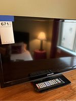 Samsung TV shown on a wooden surface with remote placed in front, black frame with Samsung logo visible