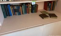 Wide view of antique books on a shelf showing two smaller books laid on the surface and many arranged upright extending left to right with visible titles and bindings