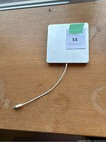 White Apple SuperDrive external DVD drive on wooden surface with USB cable extended and a label placed on top.