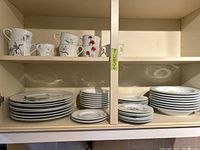 Full view of shelf showing stacks of cups, plates, and saucers with floral designs.