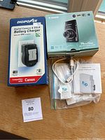 Boxed Canon PowerShot camera, Digipower charger box, Flip Video cable and manuals laid out on table